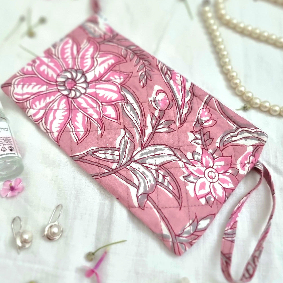 A hand-printed pink beauty bag with a zipper, adorned with a floral rose design, displayed alongside travel-sized toiletry containers and jewelry.