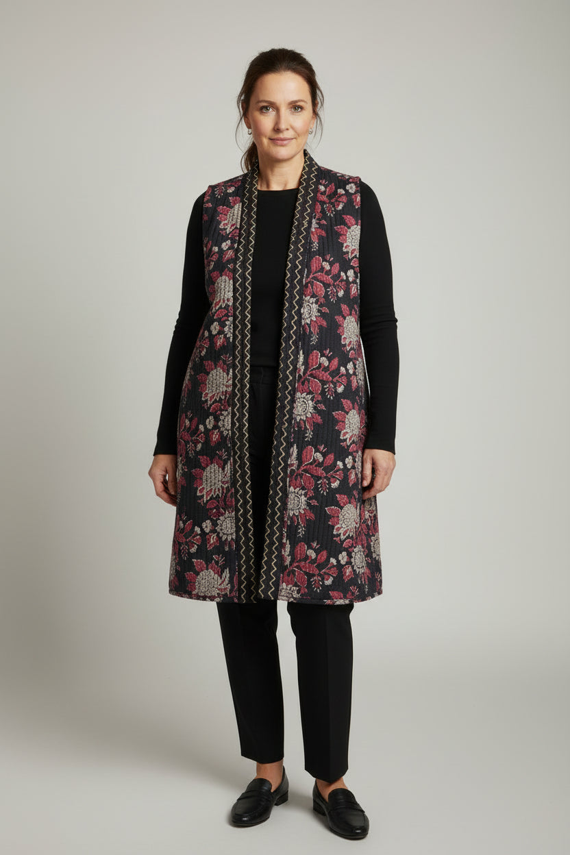 Woman wearing a floral patterned vest over a black outfit on a plain background