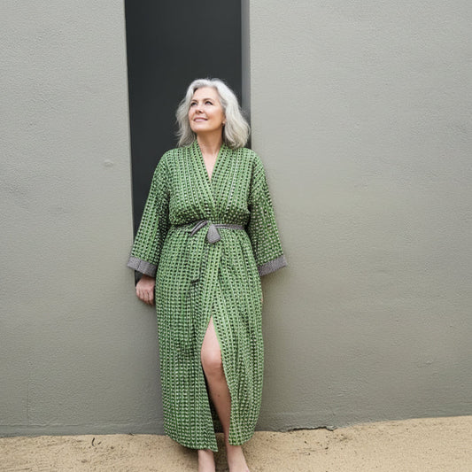 Woman wearing a green patterned robe standing against a plain wall.