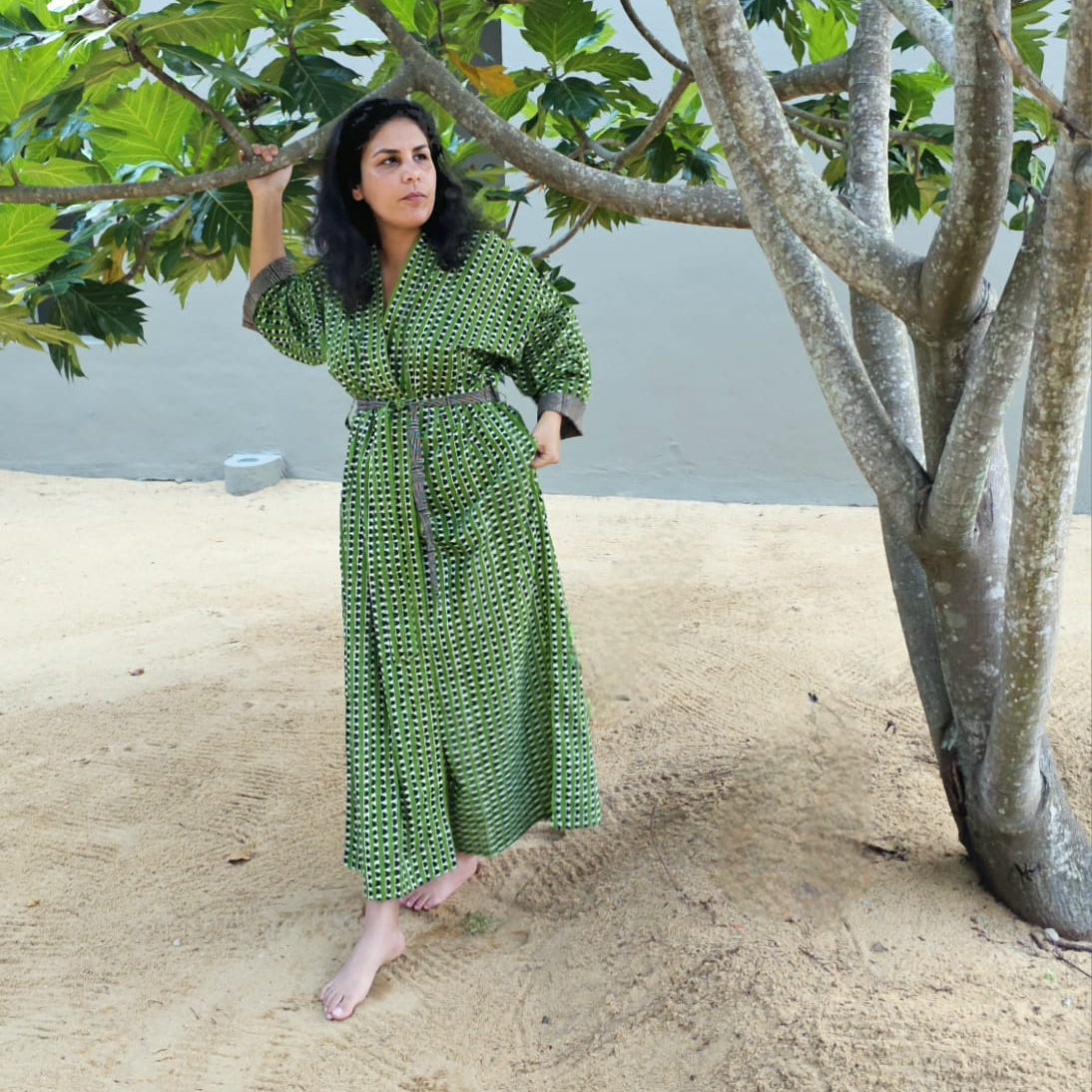 Woman in a green patterned dress standing under a tree with a beach in the background